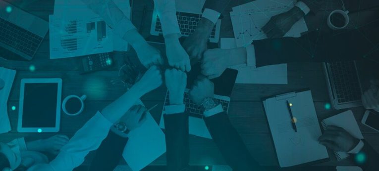 #306 (1) Na imagem, um time unindo as mãos ao redor de uma mesa. A imagem é coberta por um filtro azul e pequenos pontos de luz.